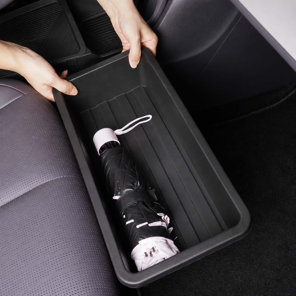 Schwarze Staubox für Leapmotor B10 unter dem Vordersitz beim Einsetzen, mit Regenschirm